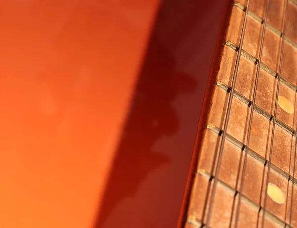 Acoustic guitar neck on an orange background. Part of a guitar on a bright background.