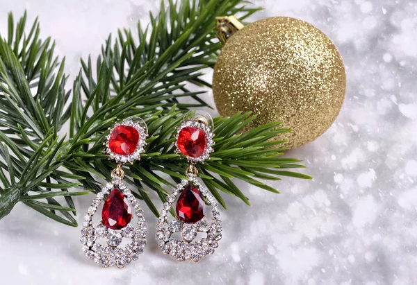 Earrings with red stones on a branch of a Christmas tree with a ball on an abstract background — Stock Photo, Image