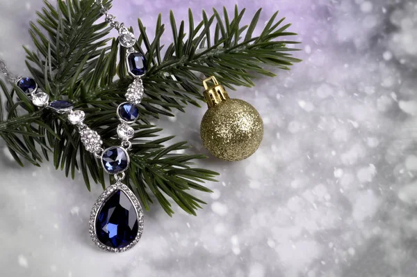 Necklace with blue stones on a branch of a Christmas tree with a ball on an abstract background — Stock Photo, Image