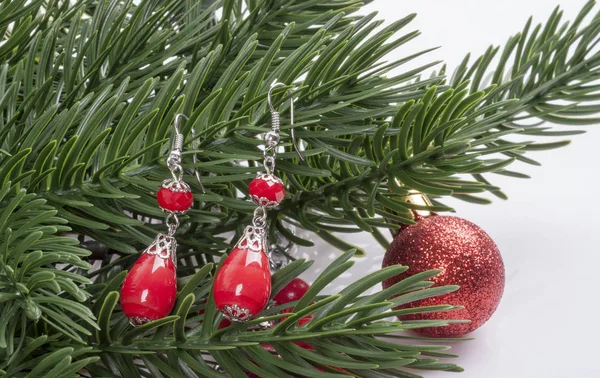Brincos com pedras vermelhas em um ramo de uma árvore de Natal com uma bola — Fotografia de Stock