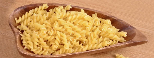 Rå pasta i en träskål närbild på ett träbord — Stockfoto