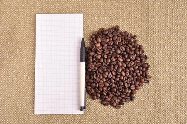 Heap of coffee beans on burlap and notepad background — Stock Photo, Image