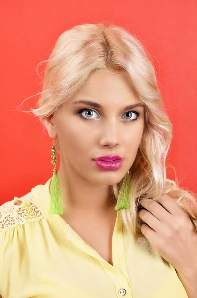 Young beautiful girl in gren earrings on an red background. — Stock Photo, Image