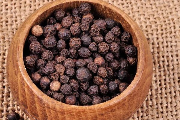 Pepper not ground in a wooden bowl on a ragged background. Stock Photo