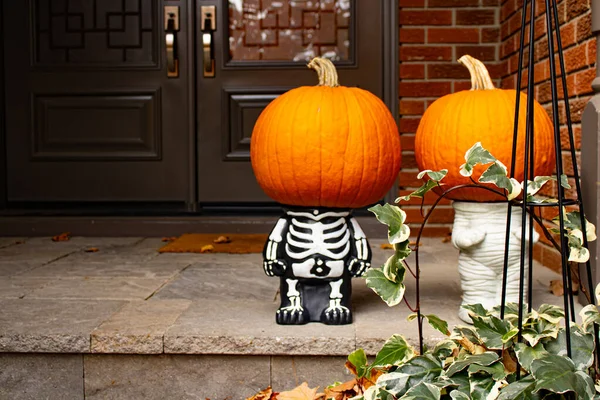 Two pumpkin-heads on small skeleton Halloween cute sculpture standing at the front doors outside of the fancy home. Season outdoor decoration — Stock Photo, Image