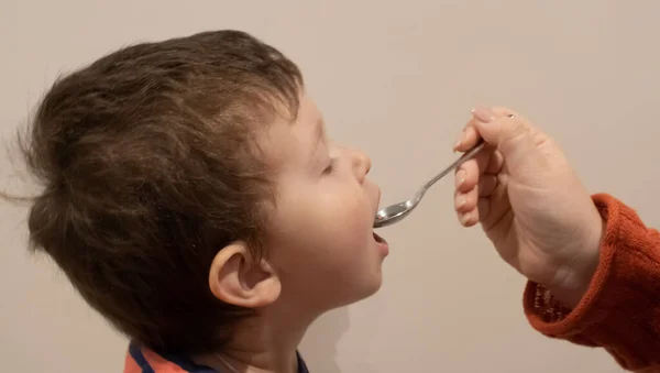 Küçük çocuk, yetişkinlerin elinden tutulan kaşıktan yiyor. Hasta bebek ilaç yiyor. — Stok fotoğraf