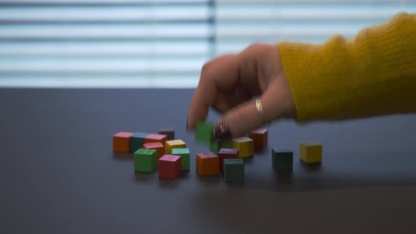 Giovane mano femminile con una manicure rossa in maglione che mescola blocchi di legno colorati e ne mette alcuni al centro . — Video Stock