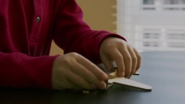 Kırmızı kazaklı küçük bir çocuk elinde oyuncak bir uçağın ahşap modelini tutuyor ve parlak bir pencerenin arka planındaki masada onunla oynuyor..