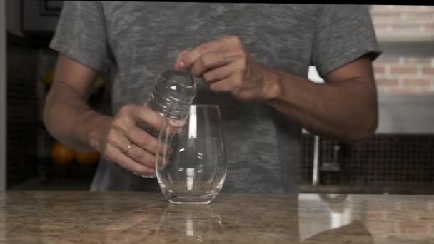 Ung man i grå t-shirt häller vatten i ett glas från en termos eller plastflaska i ett vackert modernt kök. hälsosam livsstil. Snygg man är törstig.. — Stockvideo