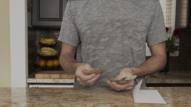 Un jeune homme tient de l'argent dans ses mains. Un gars compte les dollars canadiens qu'il a sortis de l'enveloppe. Un jeune mari raconte une grande somme d'argent. Compter l'argent dans une cuisine Payday — Video