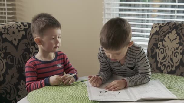 두 명의 남동생 이 식탁에 앉아서 같은 색깔로 함께 그림을 그립니다. 오빠는 행복 한 아이들을 가르치고 있습니다. 거기서 동생 과놀아나고 있습니다. 남동생은 울며 말합니다. — 비디오