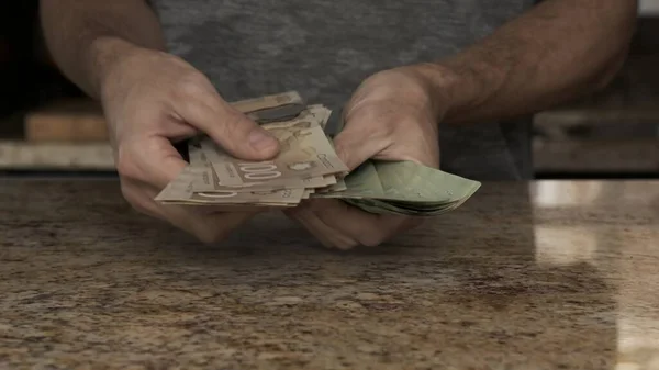 Egy fiatalember pénzt tart a kezében. Egy fickó megszámolja a kanadai dollárt, amit kivett a borítékból. Egy fiatal férj sok pénzt mesél el. Pénzt számolni a konyhában Fizetés nap Stock Kép
