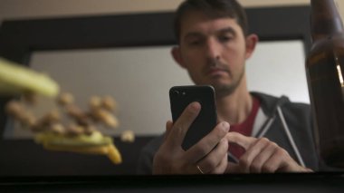 Yüksek kalitede yakın plan bir fotoğraf. Arkadaşı ya da ailesiyle telefonda sohbet eden, televizyon izleyen ve bira şişesiyle abur cubur yiyen. Mutlu zamanlar..