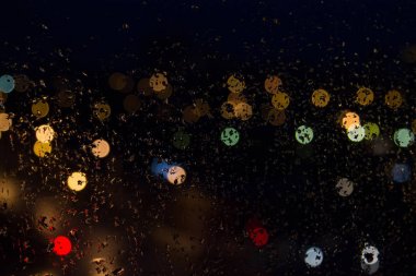 Geceleri ışıkları renkli cam üzerinde yağmur damlaları.