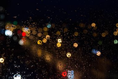 Geceleri ışıkları renkli cam üzerinde yağmur damlaları.