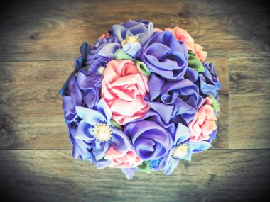 Eflatun kumaştan alınmış narin bir buket çiçeğin fotoğrafı ve siyah yuvarlak bir vignette efektiyle ahşap bir zeminde pembe.