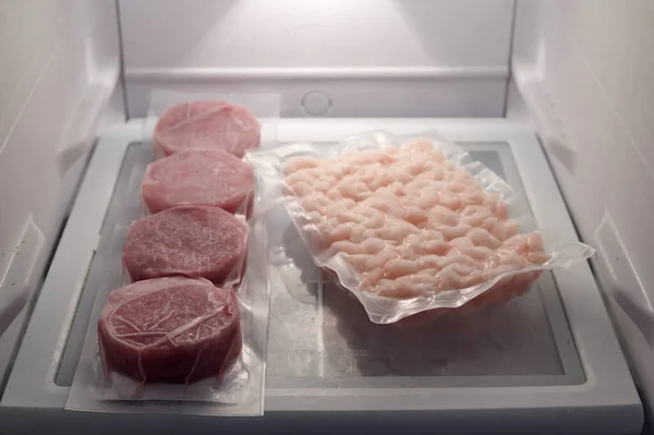 set of frozen meat and shrimp packed in plastic inside a refrigerator