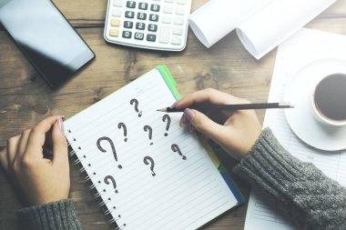 kadın eli kalem ile ile defter üzerinde soru işaretleri. telefon, kahve ve tablo hesap makinesi