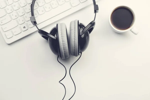 coffee cup, headphones and keyboard on wooden desktop