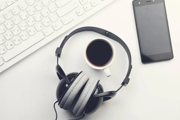 smartphone, coffee cup, headphones and keyboard on wooden desktop