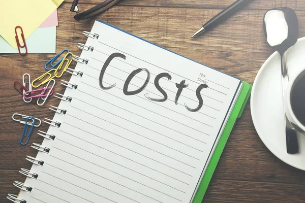Texto dos custos no caderno na tabela de trabalho — Fotografia de Stock