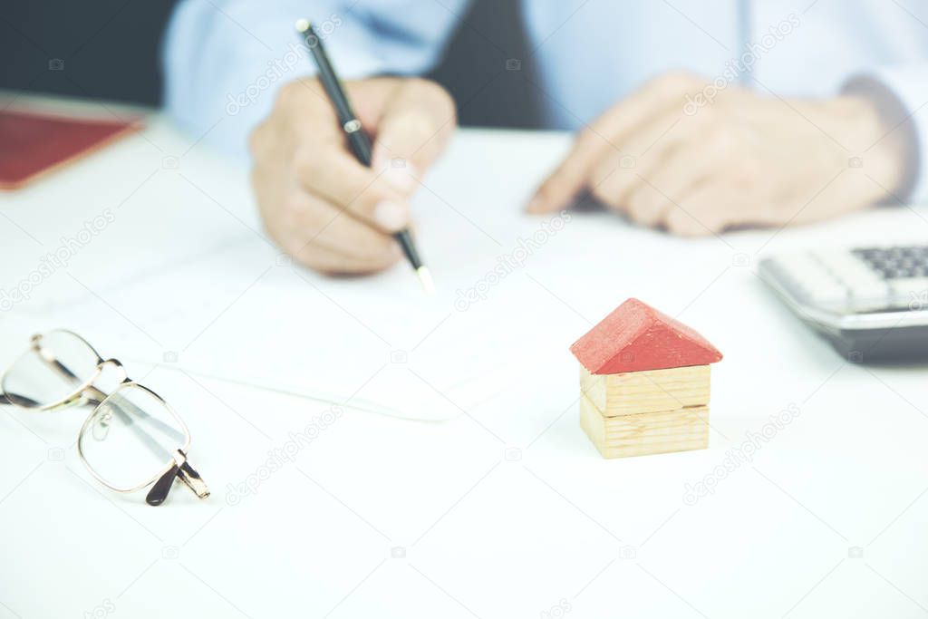 businessman signs contract behind home architectural model