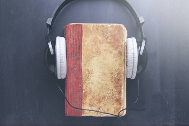 book cover and headphones over dark table clipart