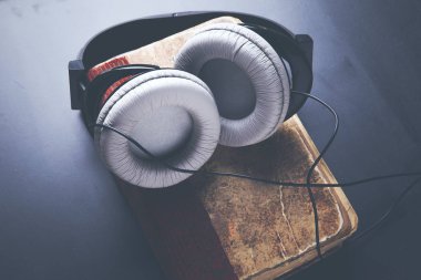 Kitap kapağı ve kulaklıklar karanlık masanın üzerinde.