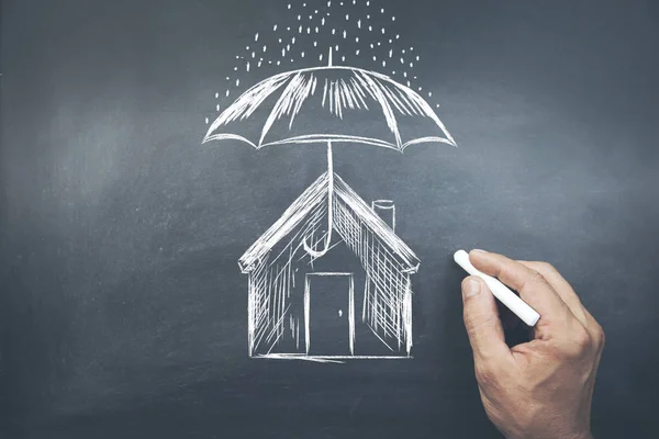 Businessman drawing umbrella over house on board — Stock Photo, Image