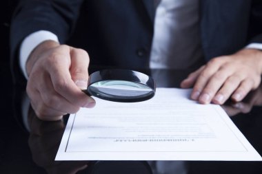 İş adamı büyüteçle belgelere bakıyor.