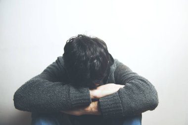 Çok üzgün bir genç adam yerde oturup ağlıyor ve yüzünü gizliyor.