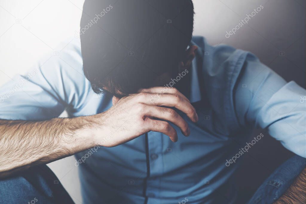 sad  man sitting on the floor crying and hiding his face