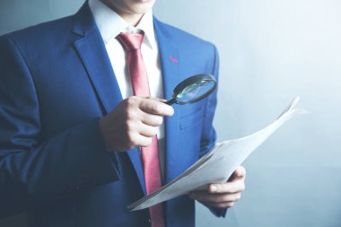 İş adamı bir büyüteçle belgeyi kontrol ediyor