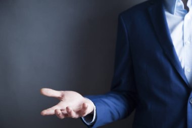 Erkek ayakta duruyor ve avuç içi açık bir şekilde elini uzatıyor.