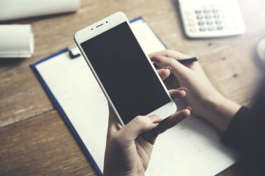 Kadın akıllı telefon ve evrakları ofis masasında.