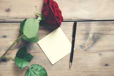 Ahşap masa zemininde kağıt olan kırmızı gül