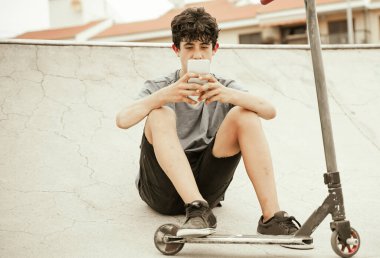 Cep telefonlu çocuk. Modern akıllı telefon teknolojisine bağımlı yoldaki genç scooter - Görüntü