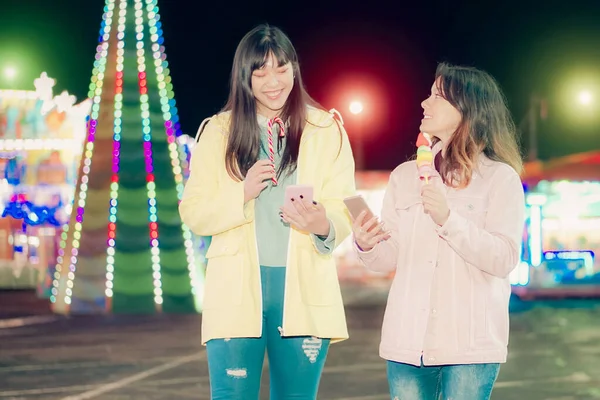 Şeker yiyen ve lunaparkta akıllı telefon arayan mutlu gençler. Genç moda Asyalı kızlar arkadaşlarıyla sohbet ediyorlar. Arkadaşlık ve Etkilendirici kavramı - Görüntü