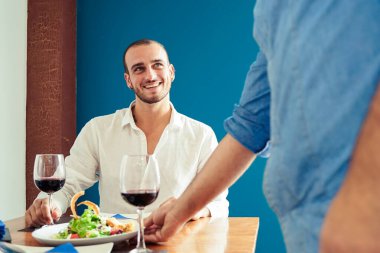 Şef restoranda müşterilere yemek sunuyor. Şefin elleri bir tabak tavuğu pirinç ve sebzeyle sunuyor. Yemek bekleyen mutlu genç adam - Görüntü