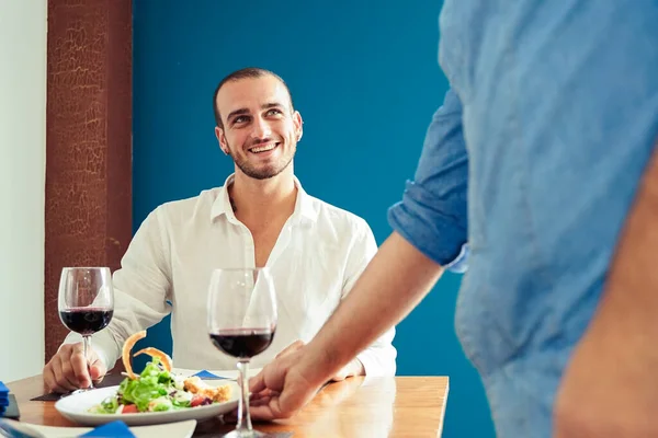 Chef presenting food to customers in the restaurant. Chefs hands presenting a plate of salad chicken with rice and vegetables. Happy young man waiting for food - Image