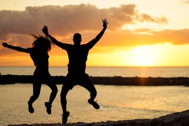 Gün batımında zıplayan arkadaş silueti. Okyanus suyunun yanında bir çift silueti. Tatil, ilişki ve aşk konsepti. Asıl gün batımı rengi - Resim