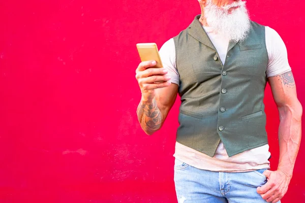 Kırmızı arka planda cep telefonu tutan beyaz bir adam resmi var. Sinirli hippi adam akıllı telefonu kulağından uzakta tutuyor. Kızgın adam izole bir şekilde telefonla konuşmak istemiyor. Görüntü.