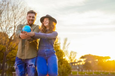 Kız kardeşi ve erkek kardeşi gün batımında diz çöküyor. Günbatımında mutlu çift. Ellerinde dünyaları olan romantik genç bir çift. Sevimli gençler, aile, aşk ve seyahat konsepti. Dünya 'ya odaklan - Resim