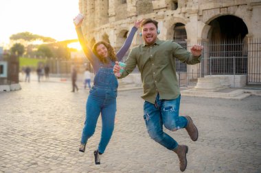 Günbatımında Roma 'da kamera zamanlayıcısıyla Colosseum' un yanında fotoğraf çeken genç bir çift. Romantik genç turistler müzik dinliyor ve lezzetli smoothie içiyorlar - Görüntü