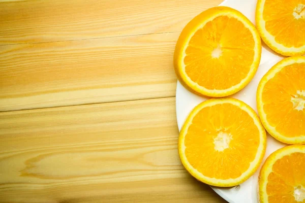 Arancione affettato su un piatto bianco su uno sfondo di legno — Foto Stock