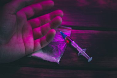 Siyah bir arka planda, üzerinde uyuşturucu yazan bir şırıngayı tutan bir elin fotoğrafını çek.