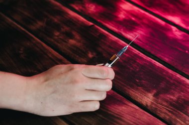 Bir adam, ahşap arka planda iğnesi olan bir şırınga tutuyor..