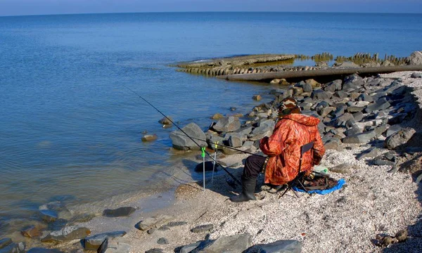 Um pescador com uma jaqueta laranja captura peixe no Mar de Azov — Fotografia de Stock