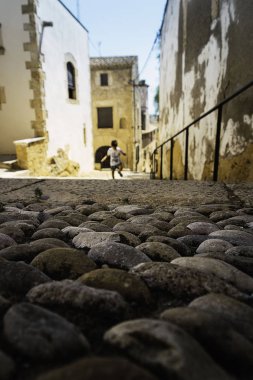 Köy sokağı taştan döşeme ve arka planda oynayan çocuk.