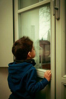 Yağmurlu bir öğleden sonra pencereden bakan bir çocuk.
